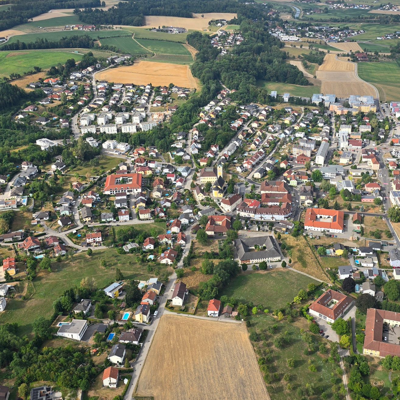 Luftaufnahme einer kleinen Stadt mit vielen Gebäuden, umgeben von grünen Feldern und Bäumen. Die Stadt hat eine Mischung aus Wohn- und Geschäftsgebäuden.