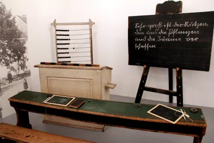 Ein altes Klassenzimmer-Setup mit einer Tafel, einem Holzschreibtisch, einem Abakus und einer kleinen Tafel auf dem Schreibtisch.