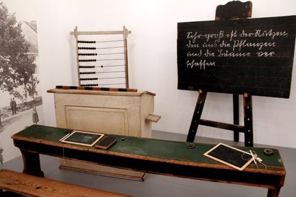 Ein altes Klassenzimmer-Setup mit einer Tafel, einem Holzschreibtisch, einem Abakus und einer kleinen Tafel auf dem Schreibtisch.