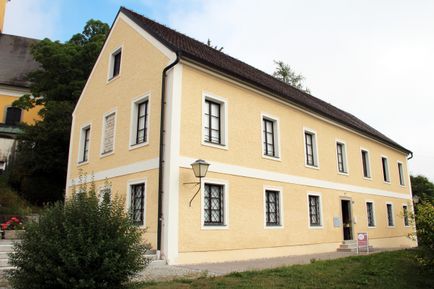 Ein gelbes Gebäude mit einem braunen Dach, mehreren Fenstern und einer Lampe an der Wand.