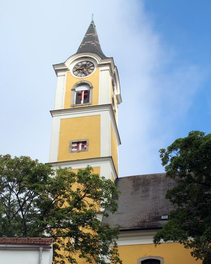 Ein hoher gelber und weißer Kirchturm mit einer Uhr und einem Schweizer Flaggensymbol darauf.