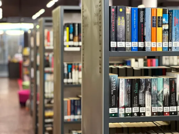 Ein Bücherregal in einer Bibliothek mit ordentlich geordneten Büchern, darunter Titel von Autoren wie Dr. E. Herr und Dr. F. Hava.