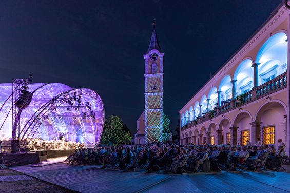 Ein Konzert im Freien bei Nacht mit einem großen Publikum, das vor einer Bühne, einem Uhrturm und einem beleuchteten Gebäude sitzt.