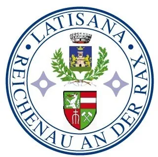 Das Emblem zeigt einen blauen Kreis mit der Aufschrift 'LATISANA REICHENHAU AN DER RAX'. In der Mitte befindet sich ein Schild mit einem grünen und weißen Wappen, flankiert von zwei lila Sternen. Über dem Schild befindet sich eine Krone und ein grünes Banner.