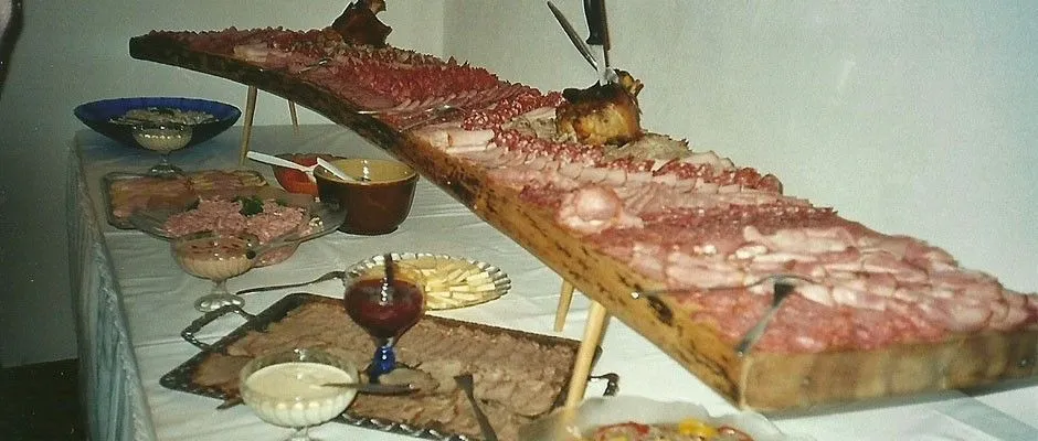 Ein langer Holztisch zeigt eine Vielzahl von Fleisch- und Käsesorten, begleitet von verschiedenen Gerichten, Schalen und einem Glas Wein.