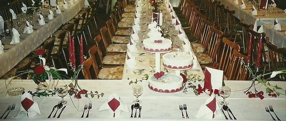 Ein langer Banketttisch für eine Hochzeitsfeier mit roten Rosen, roten Kerzen und mehreren weißen Kuchen auf einem mehrstöckigen Gestell.