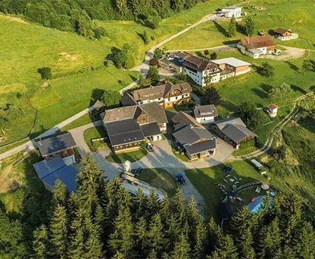 Luftaufnahme eines kleinen Dorfes in einem grünen Tal mit Häusern und einem Schwimmbad.