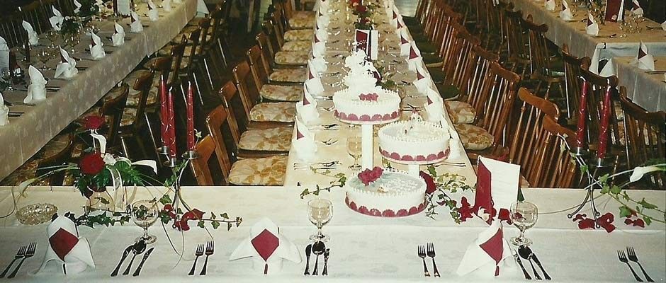 Ein langer Banketttisch für eine Hochzeitsfeier mit roten Rosen, roten Kerzen und mehreren weißen Kuchen auf einem mehrstöckigen Gestell.