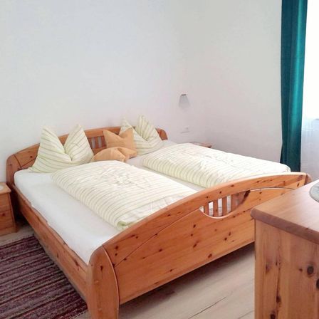 Das Innere eines Schlafzimmers mit zwei Holzbetten, Kissen und einem Nachttisch.