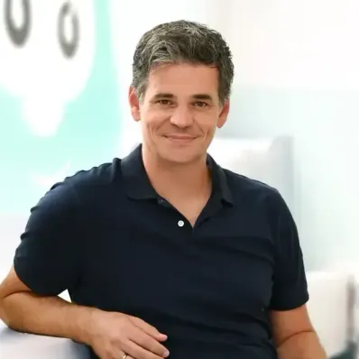Ein Mann mit grauem Haar und schwarzem Poloshirt, lächelt und posiert für ein Foto mit der Hand auf der Hüfte.