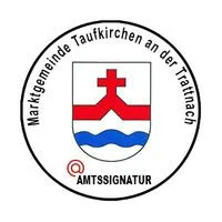 Das Bild zeigt ein kreisförmiges Emblem mit einem Kreuz in der Mitte, darunter Wellen und Text um den Umfang. Der Text lautet 'Marktgemeinde Taufkirchen an der Tratnach'. Unten unter dem Emblem steht das Wort 'AMTSSIGNATUR' in Rot.