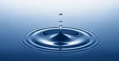 Ein Wassertropfen spritzt in eine ruhige blaue Oberfläche und erzeugt Wellen und konzentrische Kreise.