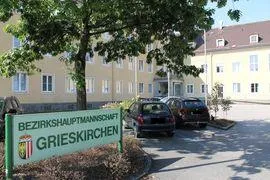 Ein Schild für Bezirksschulptmannschaft Grieskirchen vor einem Gebäude mit geparkten Autos im Hintergrund.