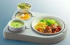 Ein Essenstablett mit drei Fächern. Eins enthält grüne Suppe, ein anderes ein Omelett, und das dritte hat ein gemischtes Gemüse- und Fleischgericht.