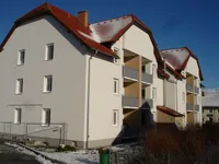 Ein modernes dreistöckiges Mehrfamilienhaus mit roten Dächern und Balkonen, in Weiß und Braun gestrichen, umgeben von Schnee und einem Zaun.