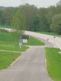 Eine Straße mit einer Kurve, leer, umgeben von grünem Gras, mit einem kleinen Gebäude und Verkehrszeichen.