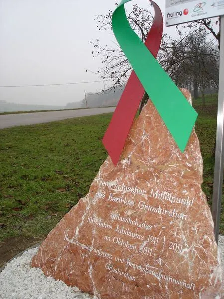 Ein Gedenkstein mit roter und grüner Schleife, umgeben von grünem Rasen. Inschriften in Deutsch markieren den 100. Jahrestag von Grieskirchen im Oktober 2011.
