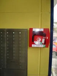 Eine gelbe Wand mit einem angebrachten Feuerlöscherkasten und einer Metallpostverteileinheit links.