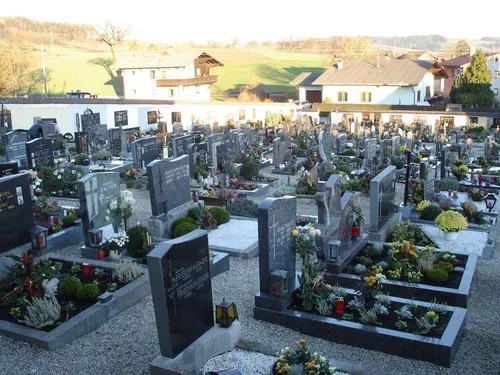 Ein Friedhof mit zahlreichen Grabsteinen und Gräbern, umgeben von kleinen Häusern und Grünflächen, mit Blumen und Pflanzen im Vordergrund.