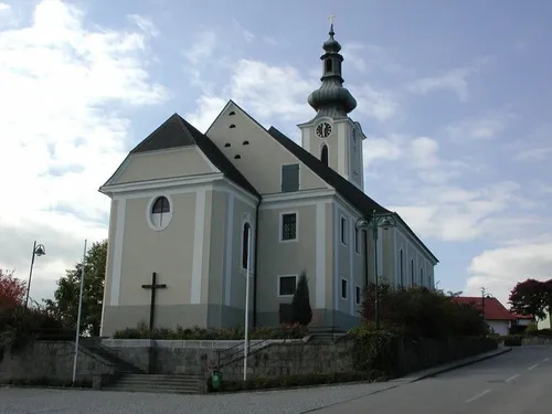 Eine Kirche mit Turm und Uhr, in einer Stadt gelegen. Sie hat ein Kreuz an ihrer Wand.