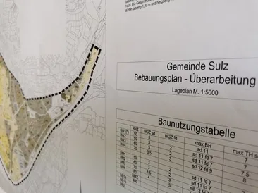 Ein Ausschnitt eines Stadtplanungsdokuments zeigt eine Karte mit einem Maßstab von 1:5000 und eine Tabelle mit Gebäudenutzungswerten. Der Titel des Dokuments lautet 'Bebauungsplan - Überarbeitung'.