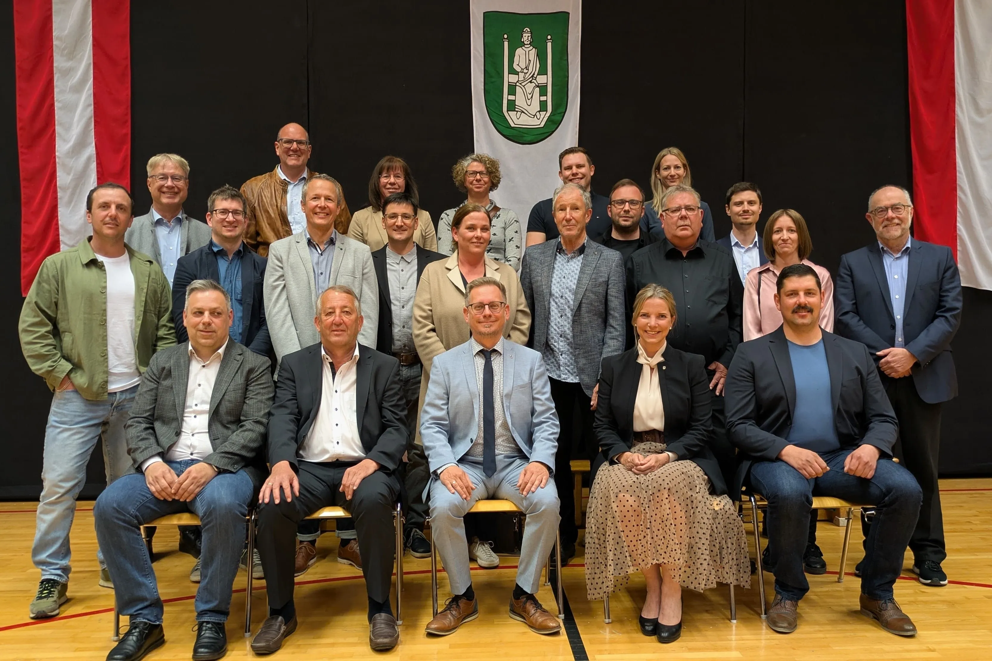 Eine Gruppe Erwachsener posiert für ein Foto mit einem Banner im Hintergrund. Sie sitzen und stehen auf Bänken, alle leger gekleidet.