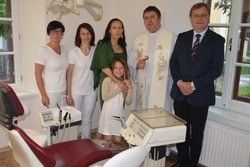 Eine Gruppe von Menschen, darunter ein Priester, steht in einer Zahnarztpraxis. Sie posieren für ein Foto mit Zahnarztgeräten im Hintergrund.