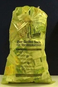 Ein gelber Plastiksack mit 'Der Gelbe Sack' und 'fur Verpackungen' darauf. Der Sack ist mit recycelbaren Materialien gefüllt. Er hat ein blau-grünes Design.