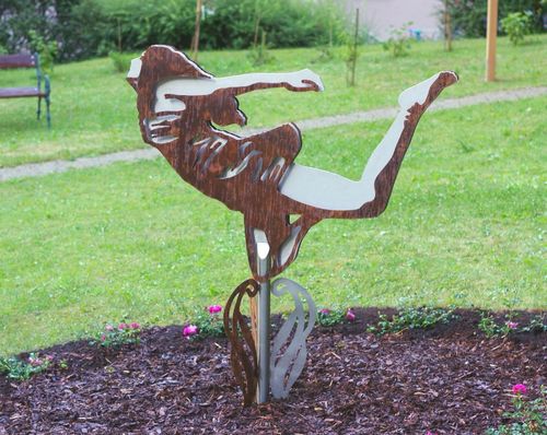 Eine Bronzeskulptur einer Frau in einer anmutigen Pose steht in einem Garten mit grünem Gras und Blumen.