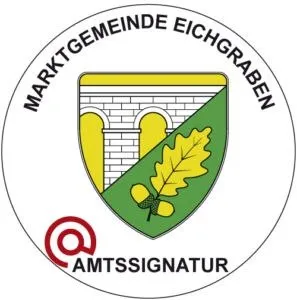 Ein rundes Emblem mit einem Schild, der eine Brücke und eine zentrale Blattdarstellung zeigt. Die Worte 'Marktgemeinde Eichgraben' sind bogenförmig über dem Schild geschrieben. Unten auf dem Schild steht 'Amtssiegel' in fetten Buchstaben. Ein Lupensymbol befindet sich auf der linken Seite des Emblems.