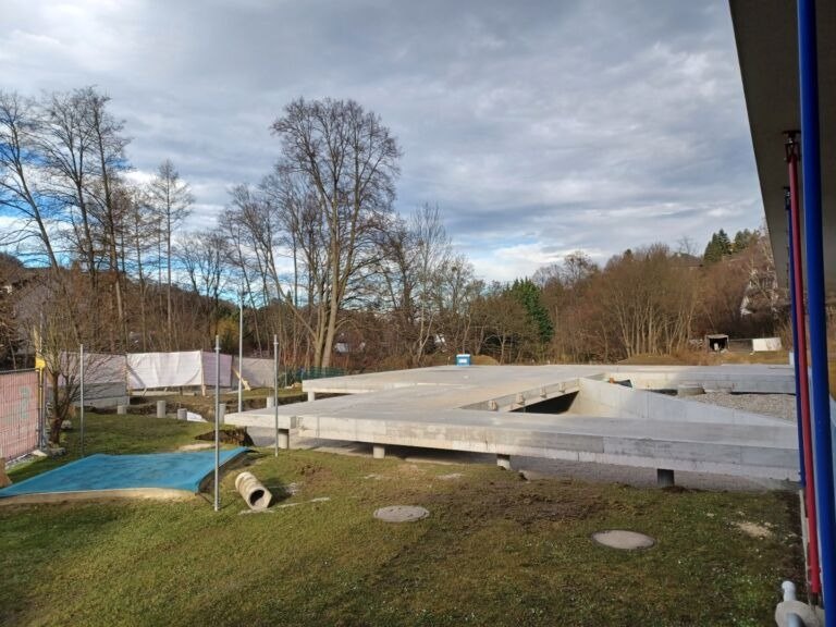 Eine Baustelle im Freien mit einer Betonplattform unter einem bewölkten Himmel, umgeben von Bäumen und Gras.