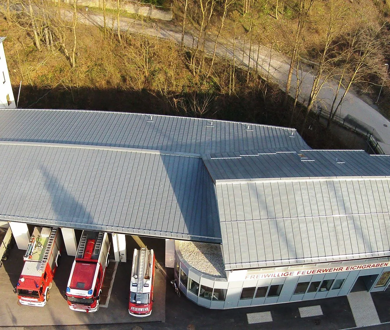 Ein Luftbild einer Feuerwehrwache mit grauen Dächern und roten Autos, die auf der Einfahrt geparkt sind. Der Text auf dem Gebäude lautet Freiwillige Feuerwehr Eich.