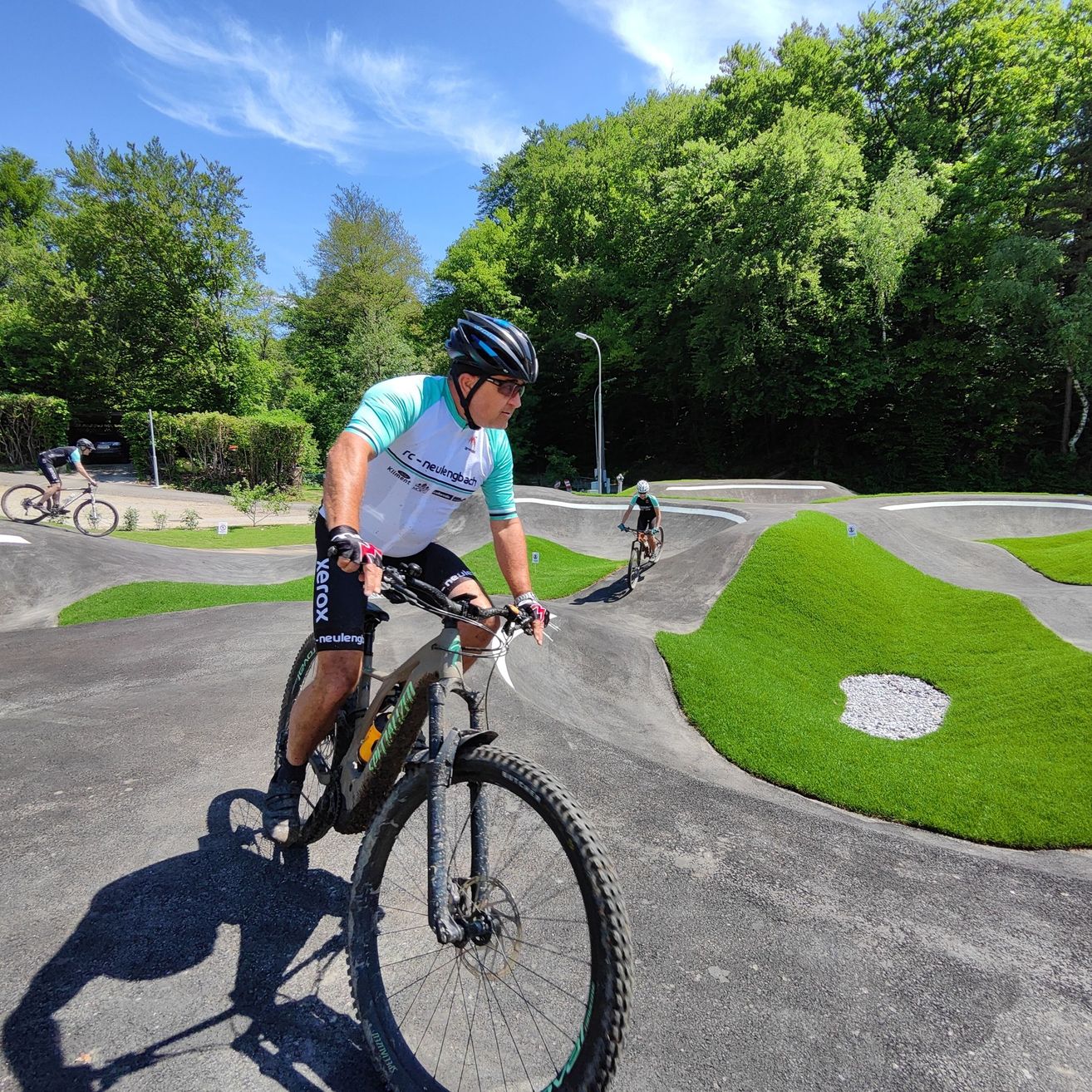 Zwei Männer fahren an einem sonnigen Tag auf einer Strecke mit Gras und Bäumen Fahrrad.