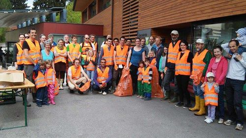 Eine Gruppe von Menschen in Warnwesten versammelt sich vor einem Gebäude. Einige halten Müllsäcke und scheinen für ein Foto zu posieren.