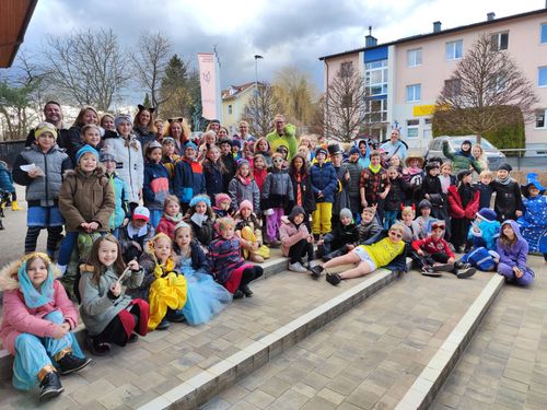 Eine Gruppe von Kindern und Erwachsenen in Kostümen posiert für ein Foto vor einem Gebäude.