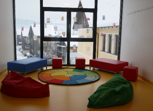 Ein gemütlicher Raum mit bunten Sitzsäcken, einem runden Teppich und einem großen Fenster mit Blick auf eine verschneite Stadt.