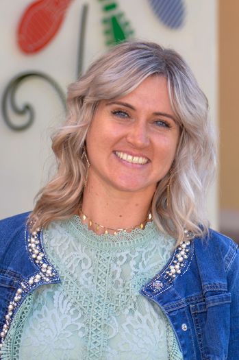 Eine Frau mit grauem Haar lächelt und trägt eine Jeansjacke mit Perlendetails und einem Spitzenoberteil.