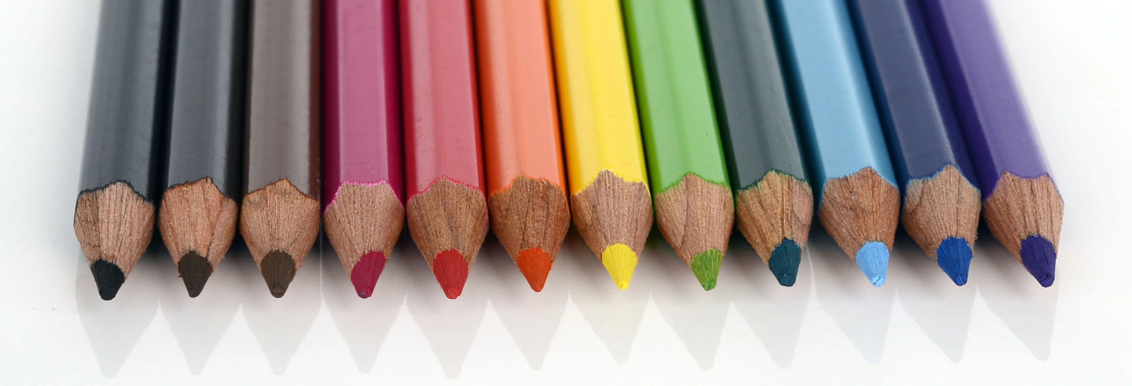 Eine Reihe von Buntstiften in verschiedenen Farben, darunter Rot, Orange, Gelb, Grün und Lila, mit nach oben zeigenden Spitzen.