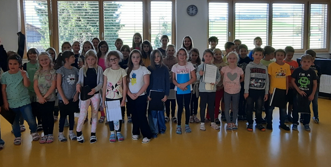 Eine Gruppe von Kindern, in Freizeitkleidung gekleidet, steht in einer Reihe in einem Klassenzimmer, hält Urkunden und posiert für ein Foto.
