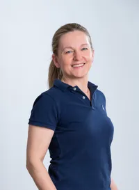 Eine lächelnde Frau in einem dunkelblauen Poloshirt posiert für ein Foto vor weißem Hintergrund.
