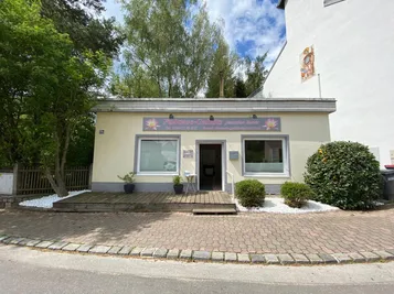 Ein kleines Gebäude mit einer Holzveranda und einem Schild, das 'Fukusase-Gabultz Jennifer Steiner' steht. Topfpflanzen sind auf der Veranda.