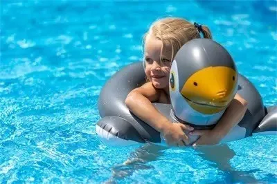 Ein kleines Mädchen in einem Badeanzug schwimmt in einem Pool mit einem grauen aufblasbaren Delphin-Schwimmflügel.