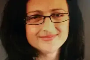 Eine lächelnde Frau mit kurzen, dunklen Haaren und Brille.