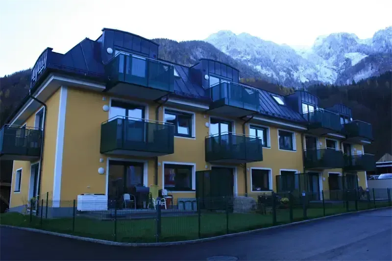 Ein Apartmentgebäude mit gelben Wänden und schwarzen Dächern steht vor einem verschneiten Berg.