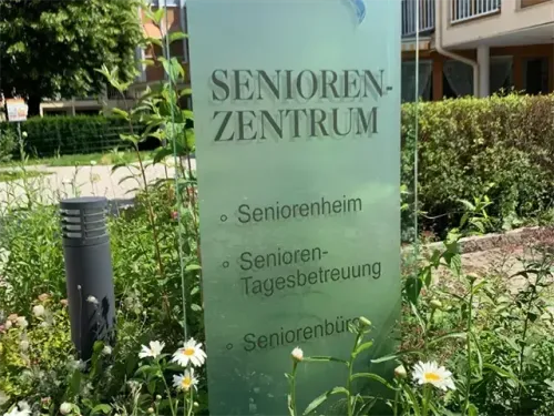 Ein Glasschild für ein Seniorenzentrum vor einem Gebäude mit Garten.