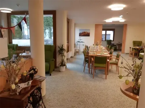 Ein Essbereich mit grünen Stühlen und Tischen ist zu sehen. Ein paar Topfpflanzen und Blumen sind auf dem Tisch platziert. Einige Stühle sind auf der rechten Seite platziert und ein Schreibtisch ist rechts aufgestellt.