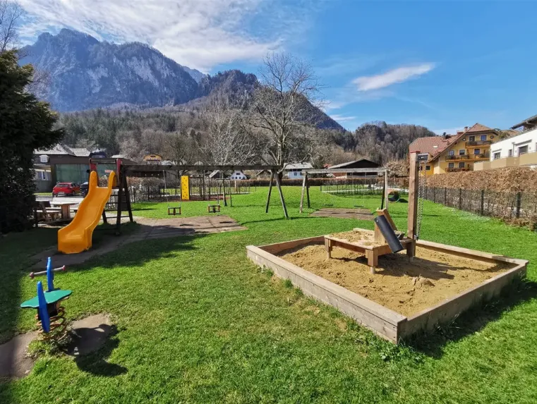 Ein Kinderspielplatz in einem Dorf mit einer Bergkette im Hintergrund.