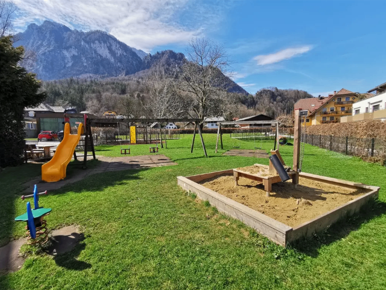 Ein Kinderspielplatz in einem Dorf mit einer Bergkette im Hintergrund.