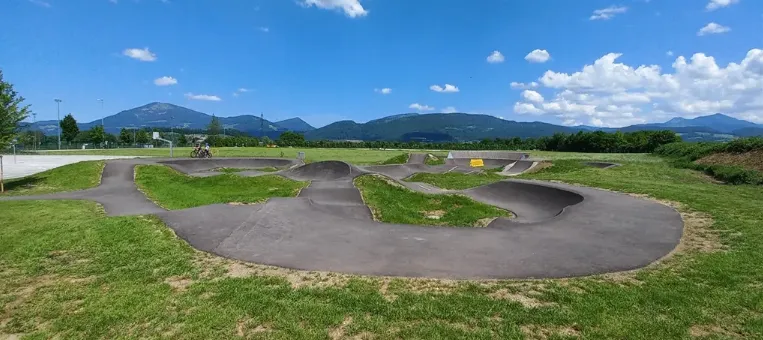 Luftaufnahme eines Skateboardparks mit Rampen und Bowls. Im Hintergrund sind Berge und ein bewölkter Himmel zu sehen.