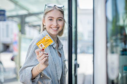 Eine Frau mit Sonnenbrille auf dem Kopf hält eine gelbe Super Cool Card in der Hand, lächelt und steht vor einer Glastür.